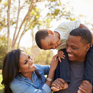 Parents Carrying Son On Shoulders As They Walk In Park